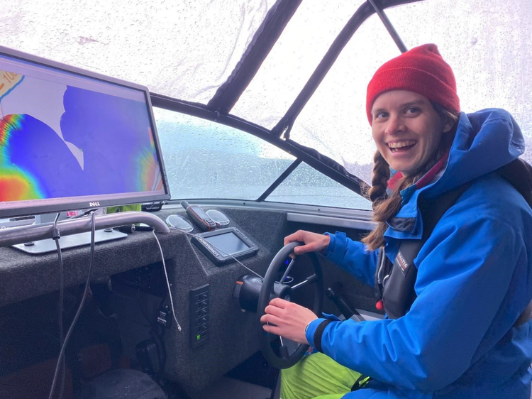 An image of Adelaine Moody smiling and driving a boat in the rain.