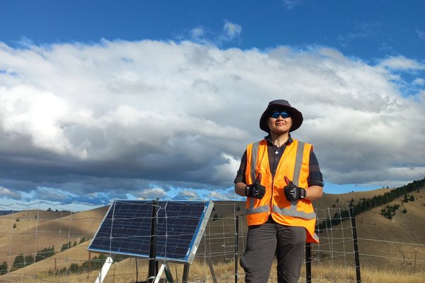 A man wearing hi vis, standing next to solar panels on a hill. Thumbs up.
