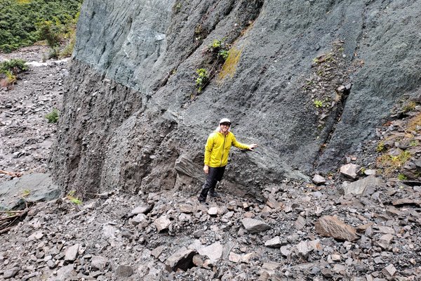 Matt standing among rock, his hand on the Alpine Fault.