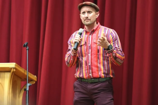 Jamie presenting in front of a large red curtain.